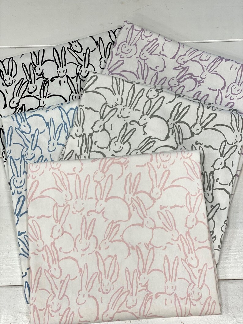 May include: Four fabric swatches with a white background and a repeating pattern of pink, black and blue bunnies. The bunnies are drawn in a simple, stylised way.