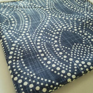 May include: A blue fabric with a white polka dot pattern. The fabric has a subtle woven texture and a slightly distressed look. The fabric is folded in half and the edges are visible.