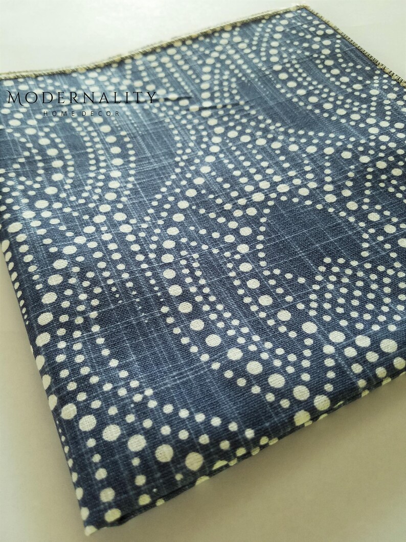 May include: A blue fabric with a white polka dot pattern. The fabric has a subtle woven texture and a slightly distressed look. The fabric is folded in half and the edges are visible.