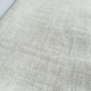 May include: Close-up of a light grey fabric with a woven texture. The fabric is smooth and has a subtle sheen. The fabric is ideal for upholstery, curtains, or other home decor projects.