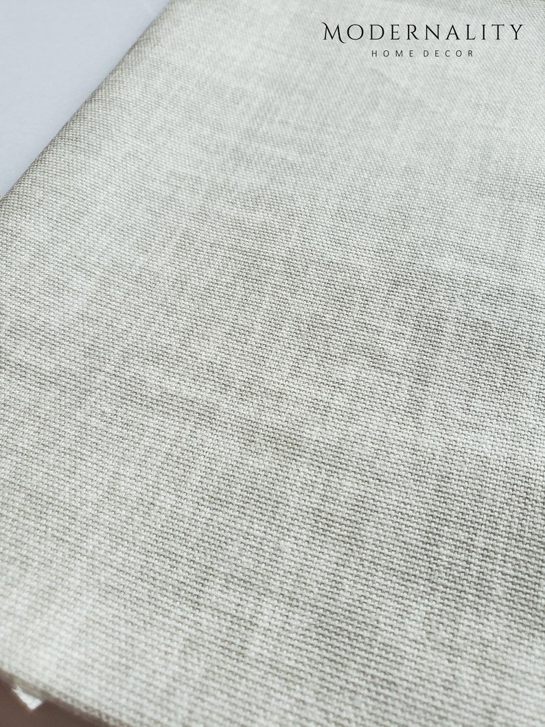 May include: Close-up of a light grey fabric with a woven texture. The fabric is smooth and has a subtle sheen. The fabric is ideal for upholstery, curtains, or other home decor projects.