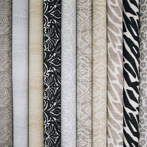May include: A collection of fabric samples featuring various patterns, including zebra stripes, leopard spots, and geometric designs. The fabrics are in shades of beige, black, and white.