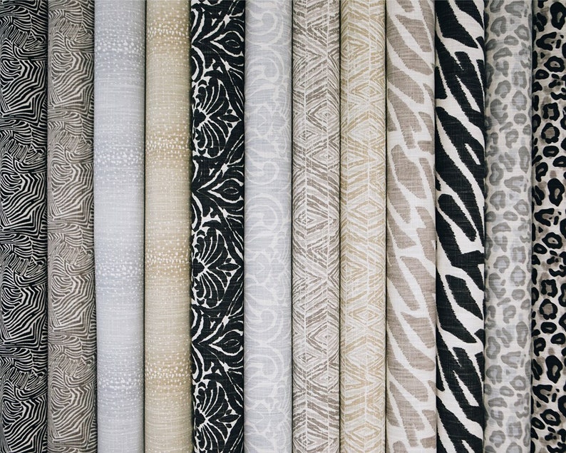 May include: A collection of fabric samples featuring various patterns, including zebra stripes, leopard spots, and geometric designs. The fabrics are in shades of beige, black, and white.