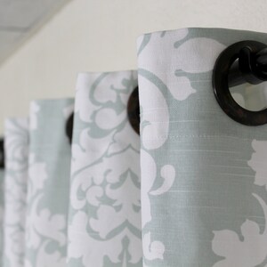 May include: A set of light blue curtains with a white damask pattern. The curtains are hung on a black curtain rod with decorative rings.