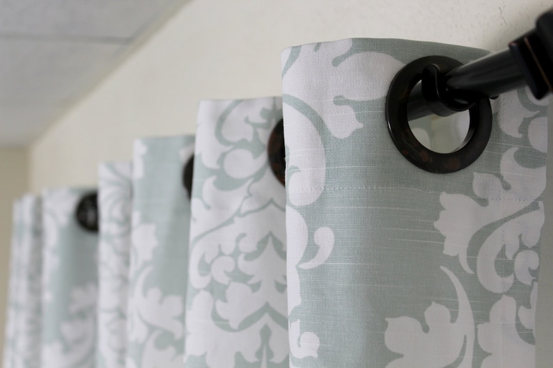 May include: A set of light blue curtains with a white damask pattern. The curtains are hung on a black curtain rod with decorative rings.