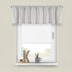 May include: A white valance with a ruffled edge hangs above a window with a white window frame. The windowsill is white and has a wooden letter K, a small gold ring, and a grey ceramic mug with pencils inside.