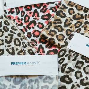 May include: Close-up of fabric swatches with a leopard print pattern in various colors, including pink, brown, and gray. The swatches are labeled with the text "PREMIER PRINTS THE ART OF FABRIC".
