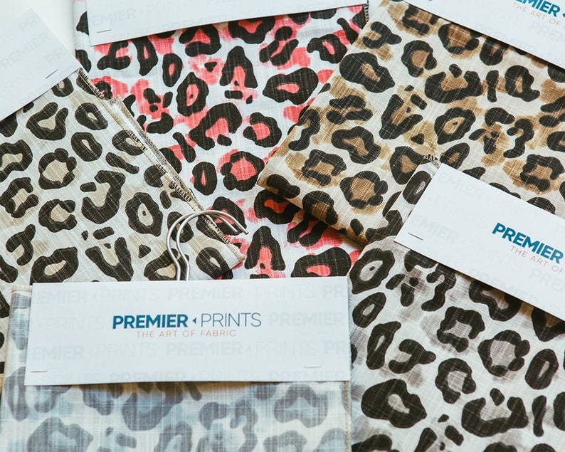 May include: Close-up of fabric swatches with a leopard print pattern in various colors, including pink, brown, and gray. The swatches are labeled with the text "PREMIER PRINTS THE ART OF FABRIC".