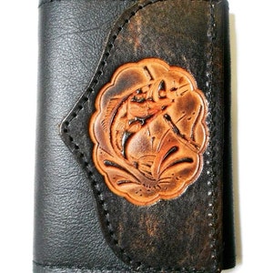 May include: A black leather wallet with a tooled design of a fish on the front. The wallet has a flap closure and a stitched edge.