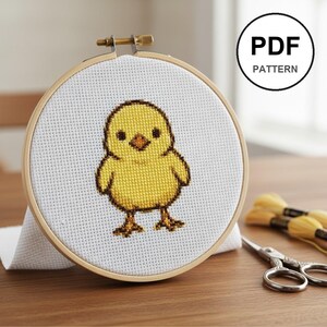 Peut inclure: Un cercle de broderie au point de croix avec un motif de poussin jaune. Le poussin est brodé sur du tissu blanc et encadré dans un cercle en bois. L'image comprend le texte "PDF PATTERN" dans un cercle.