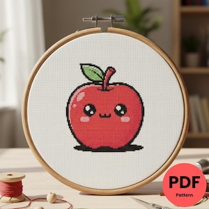 Peut inclure: Un motif de point de croix d'une pomme rouge souriante avec une feuille verte, brodé sur du tissu blanc, dans un cercle à broder en bois. La pomme a un visage souriant et des joues roses. Le texte "PDF Pattern" est sur un cercle rouge.