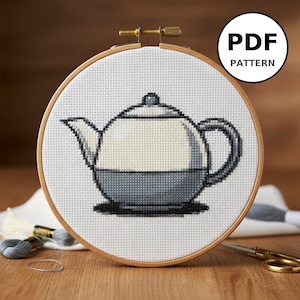 Könnte beinhalten: Kreuzstichmuster einer Teekanne in einem hölzernen Stickrahmen. Die Teekanne ist zweifarbig, mit einer hellcremefarbenen oberen Hälfte und einer dunkelgrauen unteren Hälfte. Der Text "PDF PATTERN" befindet sich in einem schwarzen Kreis.