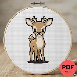 Peut inclure: Un motif de point de croix d'un cerf dans un cercle à broder en bois. Le cerf est brun et blanc avec de petits bois et de grands yeux. Le motif est sur du tissu blanc. Un cercle rouge avec "PDF Pattern" est en bas à droite.
