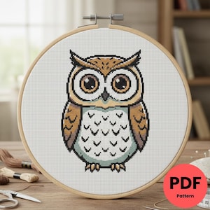 Peut inclure: Un motif de point de croix d'un hibou dans un cercle à broder en bois. Le hibou a de grands yeux ronds et est coloré dans des tons de marron, beige et blanc. Le texte "PDF Pattern" est dans un cercle rouge en bas à droite.