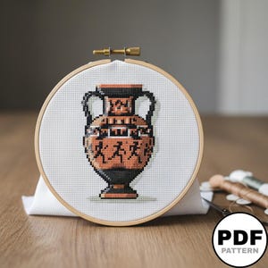 Peut inclure: Un projet de point de croix dans un tambour à broder rond en bois représentant un vase amphore de style grec. Le vase est réalisé dans des tons orange terre cuite et noir, illustrant des silhouettes stylisées en mouvement sur un tissu blanc.
