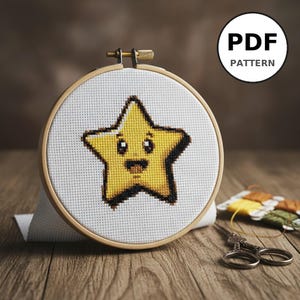 Peut inclure: Un cercle à broder au point de croix avec une étoile jaune souriante, des contours et des détails noirs. Le motif est sur du tissu blanc, maintenu dans un cercle en bois. Le texte "PDF PATTERN" est dans un cercle en haut à droite.