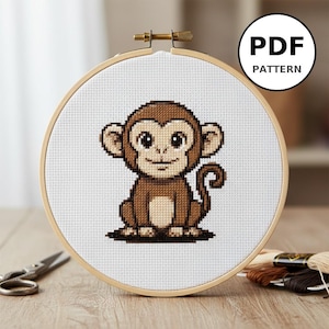 Peut inclure: Un motif de point de croix d'un singe brun dans un cercle à broder en bois. Le singe a de grands yeux et est placé sur un fond de tissu blanc. Une étiquette PDF PATTERN est dans le coin supérieur droit.