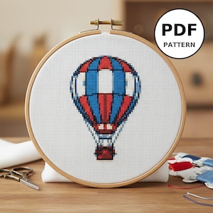 Peut inclure: Un motif de point de croix d'une montgolfière dans un cercle à broder en bois. Le motif du ballon comprend des sections rouges, blanches et bleues. Le texte "PDF PATTERN" est dans un cercle noir. Le cercle est sur une surface en bois.