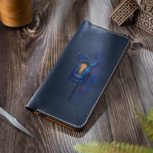 Peut inclure: Un portefeuille rectangulaire en cuir bleu marine orné d'un motif de trou de serrure en relief avec des accents bleus et fauves. Le portefeuille présente des coutures blanches visibles sur les bords et le nom TASHI gravé sur le devant.