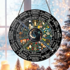May include: A circular, black decorative hanging featuring a detailed illustration of a yearly calendar. The calendar includes astrological symbols, moon phases, and seasonal elements. The design is suspended by a chain.
