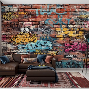 May include: A brown leather sectional sofa with a matching ottoman sits in front of a brick wall covered in colorful graffiti art. A black floor lamp stands to the right, and a patterned rug lies on the floor.