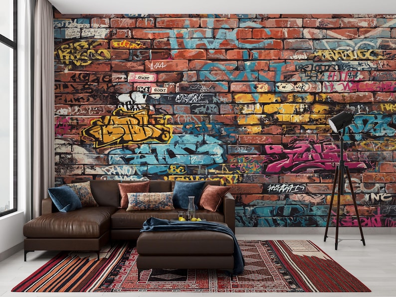 May include: A brown leather sectional sofa with a matching ottoman sits in front of a brick wall covered in colorful graffiti art. A black floor lamp stands to the right, and a patterned rug lies on the floor.
