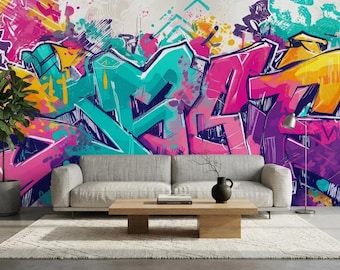 Puede incluir: Un mural de pared con arte de grafiti vibrante que presenta letras y formas abstractas pintadas con aerosol en rosa, turquesa, amarillo y morado. El diseño cubre toda la pared detrás de un sofá gris claro, una mesa de centro y una planta.