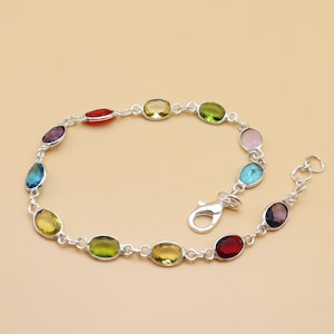 May include: A silver bracelet with a series of oval-shaped, multi-coloured gemstones. The gemstones are set in a linked chain, with colours including red, yellow, green, blue, and purple. The bracelet has a clasp closure.