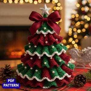 Könnte beinhalten: Ein handgehäkelter Weihnachtsbaum in Rot und Grün, verziert mit weißem Besatz und Kunstperlen. Eine bordeauxfarbene Schleife und ein silberner Stern krönen den Baum. Der Baum ist etwa 20 cm hoch.