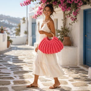 May include: A bright pink, chunky knit handbag with a rounded, pleated shape and a circular wooden handle. The bag features a thick, textured yarn construction with a wide, open-top design, showcasing a vibrant, solid color that contrasts with the neutral tone of the clothing.