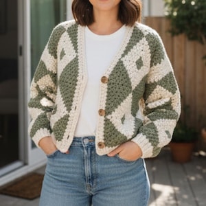 May include: A cream and olive green crochet cardigan with a diamond pattern. The button-down sweater has three brown buttons and is worn over a white t-shirt and blue jeans. The cardigan is a cozy, handmade garment.