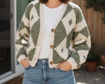 Könnte beinhalten: Eine cremefarbene und olivgrüne Häkeljacke mit Rautenmuster. Der Cardigan mit Knöpfen hat drei braune Knöpfe und wird über einem weißen T-Shirt und einer blauen Jeans getragen. Die Strickjacke ist ein gemütliches, handgefertigtes Kleidungsstück.