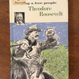 May include: A vintage book cover with an illustration of Theodore Roosevelt on horseback, raising his fist. The title reads "Roosevelt: A Free People" with the author's name below. The cover has a blue and green background.