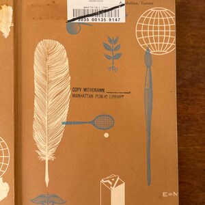 May include: A vintage book cover with a tan background and blue and white illustrations. The cover features a large feather, a tennis racket, a globe, and a paintbrush. Text includes "COPY WITHDRAWN" and "MANHATTAN PUBLIC LIBRARY".