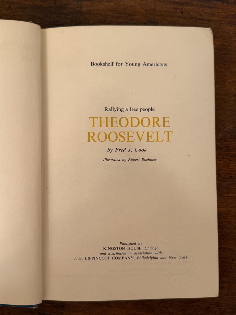 May include: An open book displaying the title page of "Theodore Roosevelt" by Fred J. Cook. The book is from the "Bookshelf for Young Americans" series. The title and author's name are in a gold font.