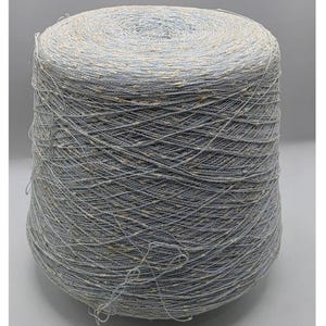 May include: A large cone of light blue yarn featuring a textured appearance with small, evenly distributed tan flecks throughout the thread. The yarn is wound tightly in a cylindrical shape, showcasing a consistent color and speckled pattern.