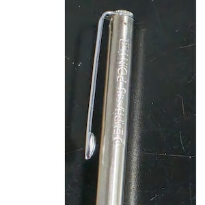 May include: A silver-toned metal pen featuring a long, slender pocket clip attached to the cap. The side of the pen is engraved with the text EMPHASIS POINTER in capital letters, positioned vertically along the cylindrical body of the writing instrument.
