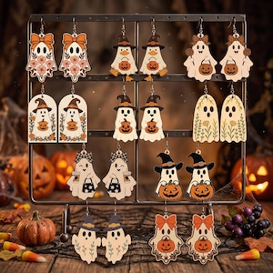 May include: A collection of ten pairs of dangling earrings featuring various ghost illustrations with Halloween themes, including pumpkins, witch hats, bows, and floral patterns, all displayed on a metal rack with hooks.