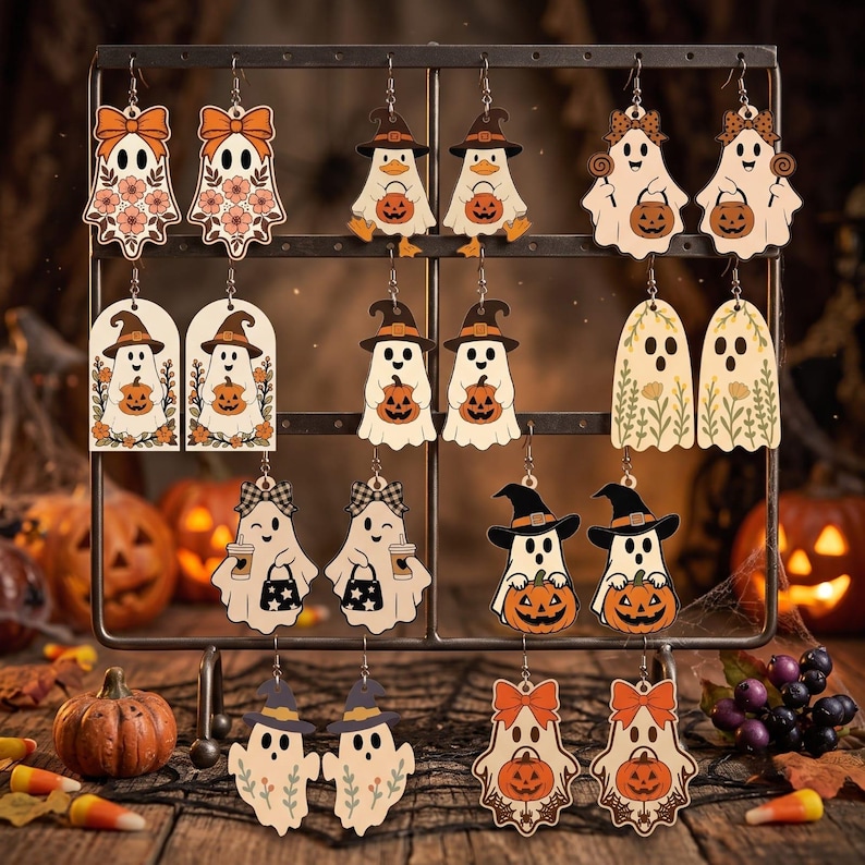 May include: A collection of ten pairs of dangling earrings featuring various ghost illustrations with Halloween themes, including pumpkins, witch hats, bows, and floral patterns, all displayed on a metal rack with hooks.