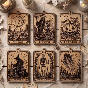 May include: A set of six rectangular wooden tarot cards featuring engraved illustrations of The Moon, The Death, The Pumpkin, The Witch, The Skeleton, and The Banshee. Each card has a small circular hole at the top for hanging and detailed black line art.