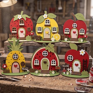 Può includere: Sei casette decorative in legno a forma di frutta, tra cui fragola, limone, mela, ananas, anguria e un'altra mela. Ogni pezzo include porte, finestre, recinzioni e dettagli floreali in miniatura, con alcuni cartelli che riportano la scritta Welcome.