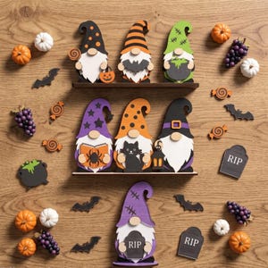 May include: A collection of wooden Halloween-themed gnomes and decorative accents including pumpkins, grapes, bats, cauldrons, and tombstones with the text RIP. The gnomes feature various hats with patterns like stripes, polka dots, and stars.