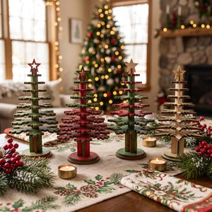 May include: Four decorative tabletop Christmas trees made of layered wooden snowflake shapes. Three trees are painted in shades of green and red, while the fourth is natural wood. Each tree is topped with a star and stands on a circular base.