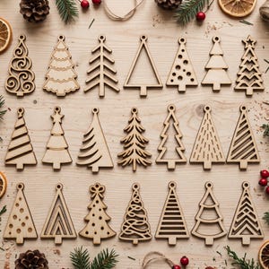 May include: A collection of twenty-one light-colored wooden Christmas tree ornaments arranged in three rows. Each ornament features a unique laser-cut design, including geometric patterns, swirls, dots, and open-frame tree silhouettes.