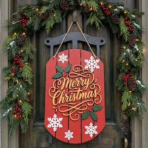 May include: A red wooden sled wall hanging featuring the gold script text Merry Christmas, white snowflake cutouts, and green holly leaf accents with red berries, suspended by a rope against a dark door with a pine garland.