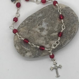 May include: A silver chain bracelet with red glass beads and a silver cross charm.