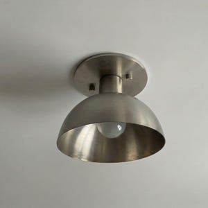 May include: A brushed nickel ceiling light fixture with a semi-spherical shade and a round mounting plate. The light bulb is visible inside the shade. The fixture is mounted on a white ceiling.