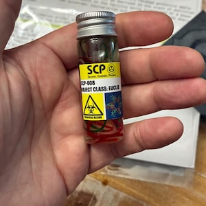 May include: A small clear glass vial with a silver screw-top lid containing red and green coiled filaments. A yellow and white label features the text SCP, SCP-008, OBJECT CLASS: EUCLID, and a yellow biological hazard warning symbol.