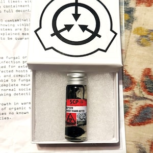 Peut inclure: Un petit flacon en verre transparent avec un bouchon à vis argenté contenant une substance sombre, étiqueté avec un autocollant rouge et blanc SCP-020 Object Class: Keter. Le flacon est logé dans de la mousse blanche dans une boîte blanche.