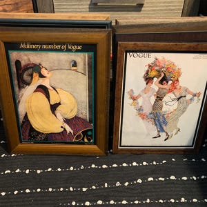 May include: Two framed vintage Vogue magazine covers. One features a woman in a yellow and purple dress with the text "Millinery number of Vogue". The other shows three women with floral headdresses.
